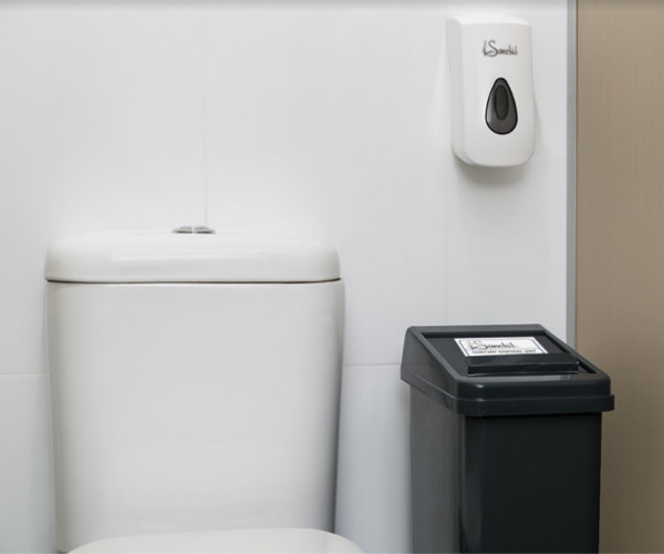 A sanitary bin next to a toilet inside a cubicle.